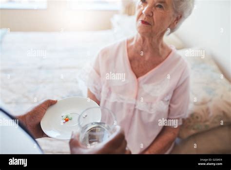 Senior Woman Sitting On Bed And Home Care Nurse Giving Medication Hand Of Nurse Giving Pills To