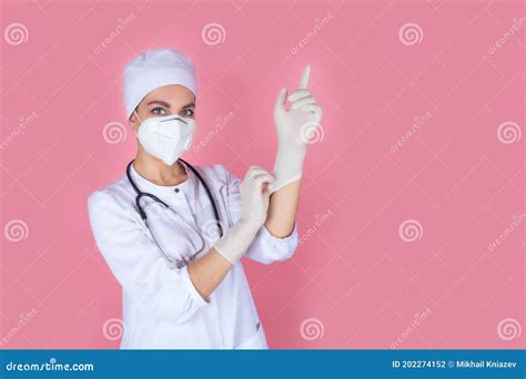 a beautiful woman doctor or nurse in a medical mask and cap puts on protective gloves stock