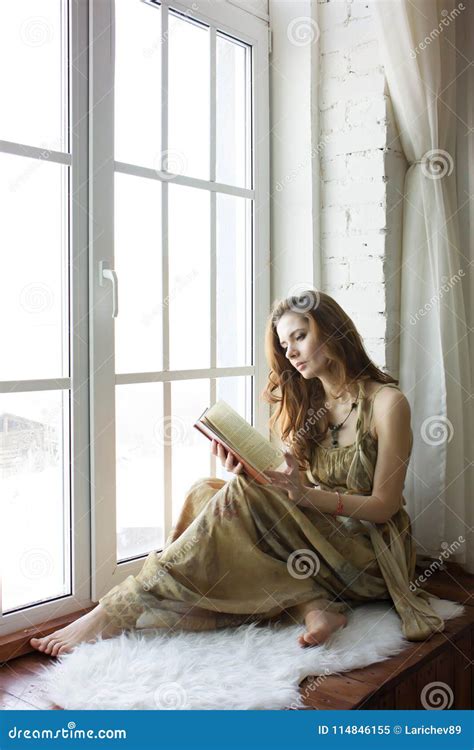 Beautiful Young Woman Sitting At A Window And Reading Book Stock Image
