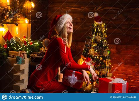 Happy Smiling Young Blonde Woman In Red Dress And Santa`s Hat At Christmas Decorated Background