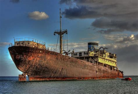 An Old Rusted Ship Sitting In The Middle Of The Ocean Under A Cloudy Sky