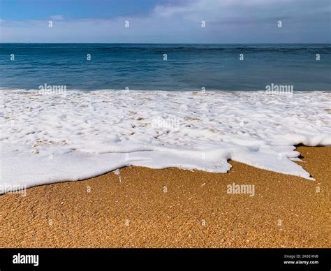 Low Angle View Of Ocean Wave Washing Up Onto Sandy Beach Under A Blue