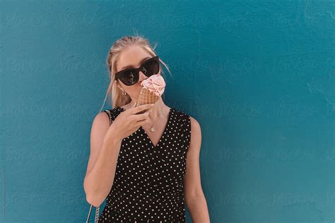 A Beautiful Young Blonde Woman Eating A Pink Ice Cream Cone In The