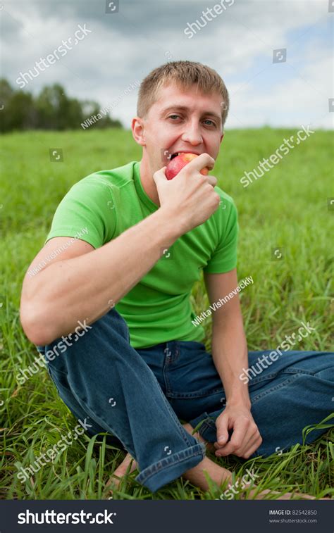 Young Man Sitting On The Grass And Eats An Apple Stock Photo 82542850
