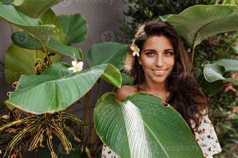Green Eyed Brunette Woman With Flower In Her Hair Looks Into Camera