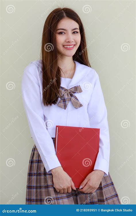 chica linda y joven que usa el estilo coreano japonés escolar uniforme sosteniendo libro y posar