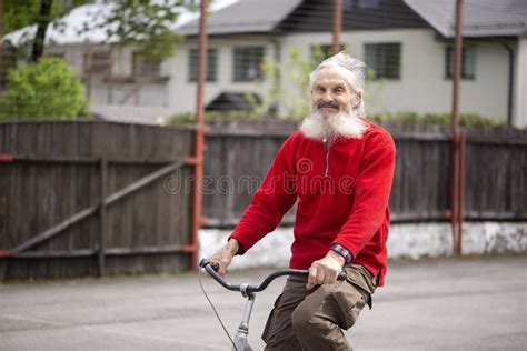 Old Bearded Man Rides A Bicycle Wearing A Red Sweater Hair Flowing In