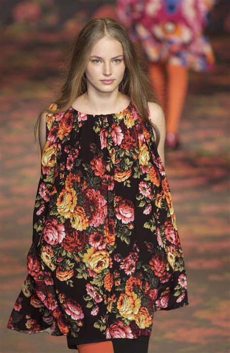 A Model Walks Down The Runway In A Black Floral Print Dress With Orange