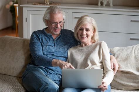 Senior Couple Sitting On Comfortable Couch Watching Video On Computer