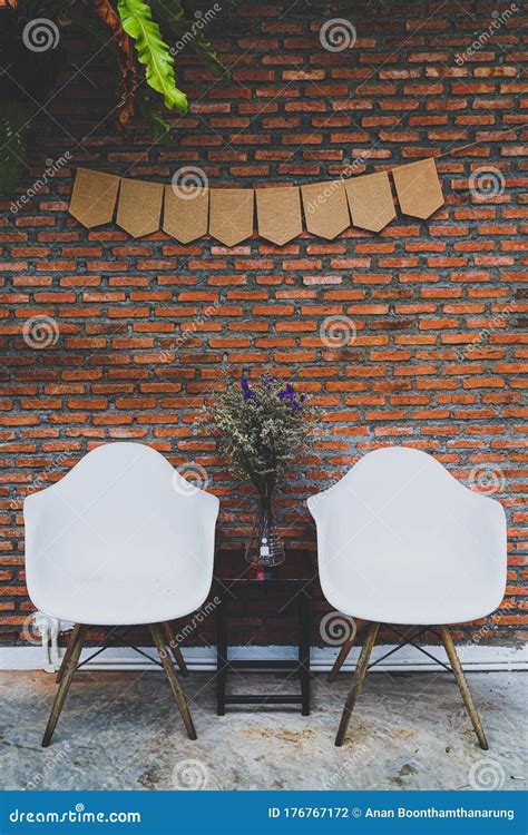 Two White Chairs With A Table Were Set In Front Of The Red Brick Wall