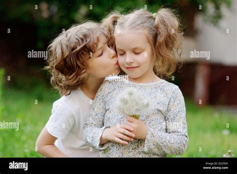 Boy Kisses Girl With Dandelions In Her Hand Into The Cheek Stock Photo