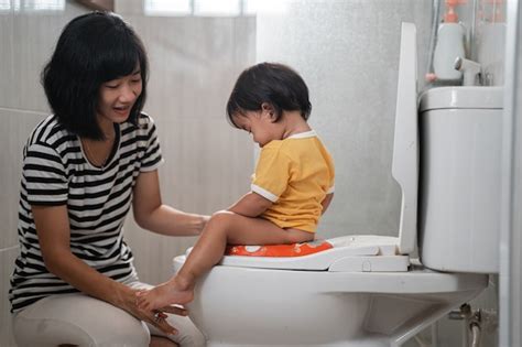 premium photo asian woman help her daughter to sit on the toilet while peeing at bathroom