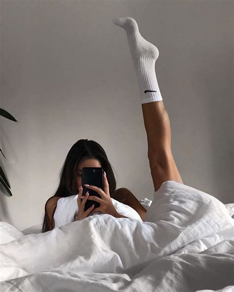 A Woman Laying In Bed With Her Legs Up And Taking A Selfie On Her Phone