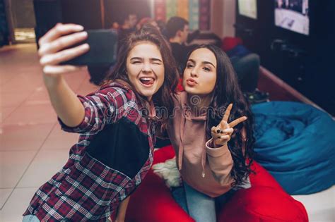 Two Young Women Taking Selfie On Phone Camera And Posing In Playing