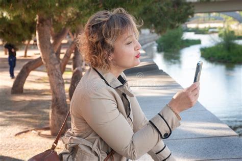 pretty and elegant middle aged woman making a selfie with her mobile phone in a park stock image