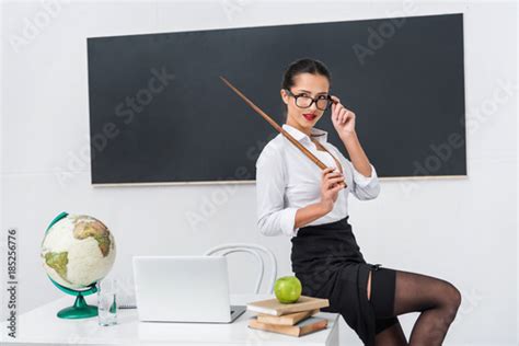 Babe Sexy Teacher In Stockings With Pointer Sitting On Desk In Front Of Chalkboard Stock Photo