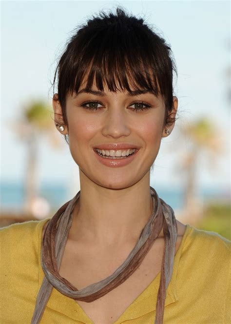 A Woman With Short Brown Hair Wearing A Yellow Shirt And Necklace Smiling At The Camera