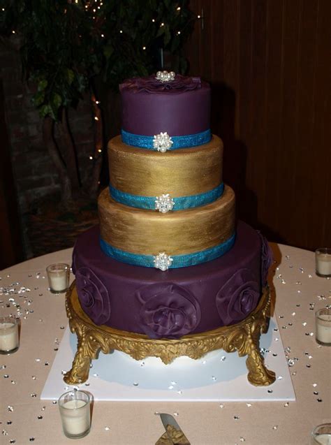 A Purple And Gold Wedding Cake Sitting On Top Of A Table Next To Some