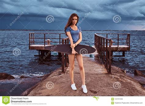 Portrait Of A Sensual Girl Holds A Skateboard While Standing On The Beach Is Enjoying Amazing