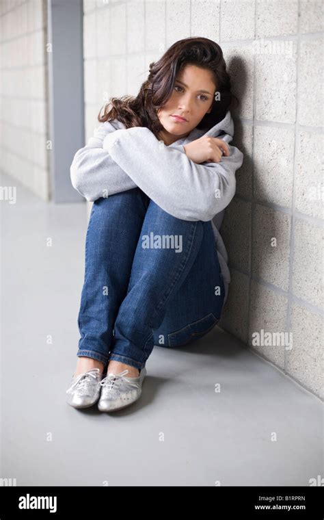 Young Woman Sitting Sadly On The Floor Leaning Against A Wall Stock