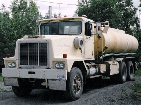 A Large White Truck Parked On The Side Of A Road Next To Trees And