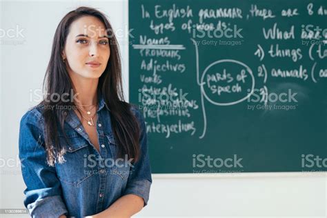 Smiling Female Teacher Standing In Front Of Blackboard In Classroom