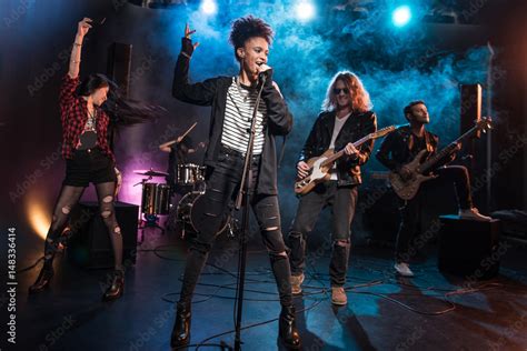 Female Singer With Microphone And Rock And Roll Band Performing Hard