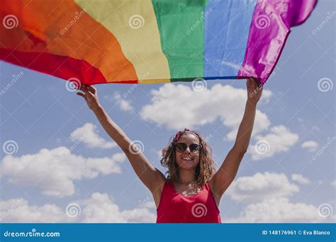 Woman Holding The Gay Rainbow Flag Over Blue And Cloudy Sky Outdoors