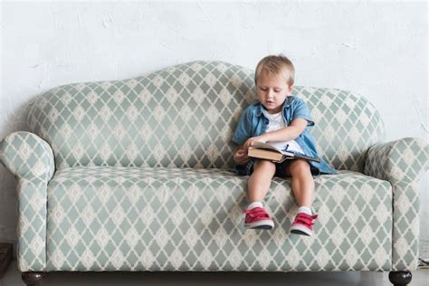 Niño Sentado En El Sofá Pasando Las Páginas Del Libro Foto Gratis