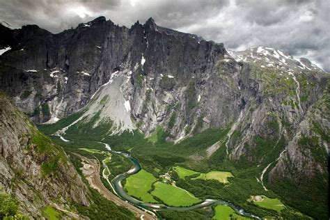 The Mountains Are Covered In Green Grass And White Clouds With A River