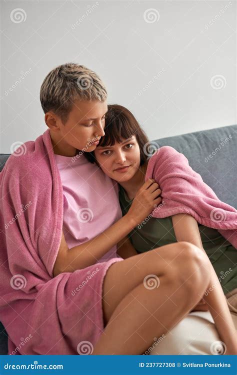 lesbianas sentadas bajo la toalla y abrazadas en el sofá en casa foto de archivo imagen de