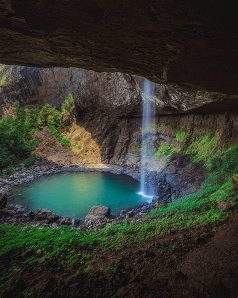 A Waterfall Is Coming Out Of A Cave With Blue Water And Green Grass In