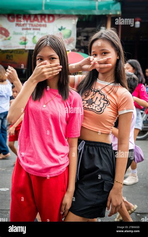 Two Young Filipino Girls Make A Cheeky Pose And Hand Signal During A