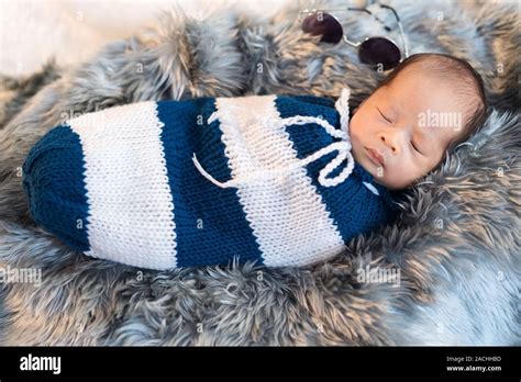 Newborn Baby Boy Sleeping And Swaddled In A Knit Wrap On A Bed Stock