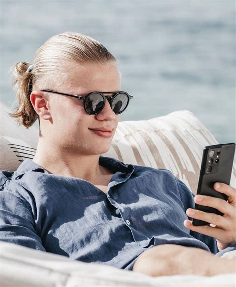 A Woman Wearing Sunglasses Is Looking At Her Cell Phone While Sitting
