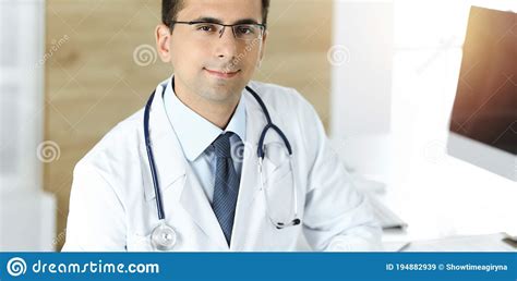Man Doctor Sitting At The Desk At His Working Place And Smiling