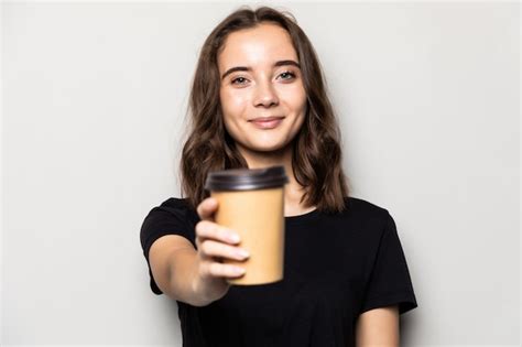 젊은 아름 다운 여자는 회색 벽에 고립 된 커피의 흰색 컵을 제공합니다 무료 사진