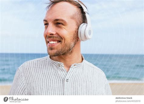glücklicher entspannter mann mit kopfhörern genießt den sommertag am strand ein lizenzfreies