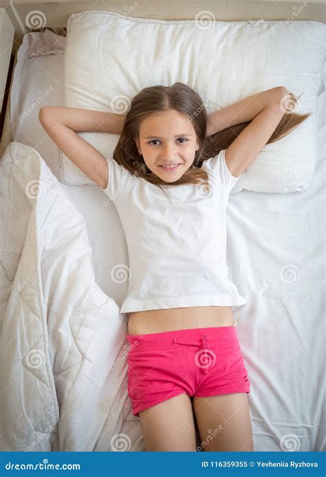 Portrait Of Beautiful Smiling Girl In Pajamas Lying On Bed And Looking