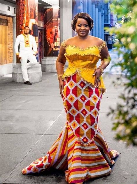 A Woman Is Standing On The Sidewalk Wearing A Colorful Dress And Gold Jewelry With Her Hands In