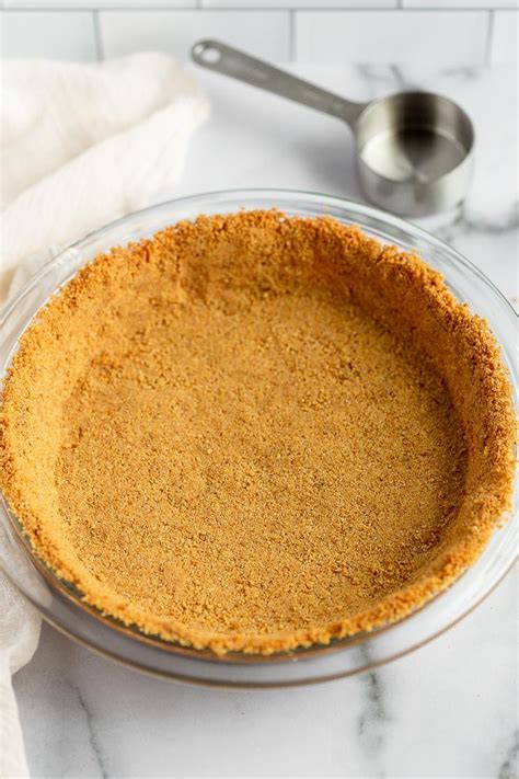 A Baked Graham Cracker Crust In A Pie Plate With A Measuring Cup Behind