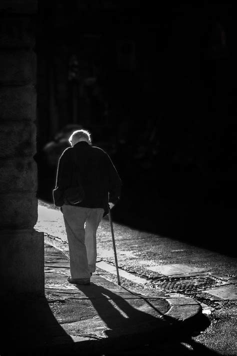 An Old Man Walking Down The Street With His Cane In Hand And Shadow On