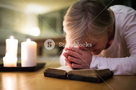 Senior Woman Kneeling On The Floor Praying With Hands Clasped Together