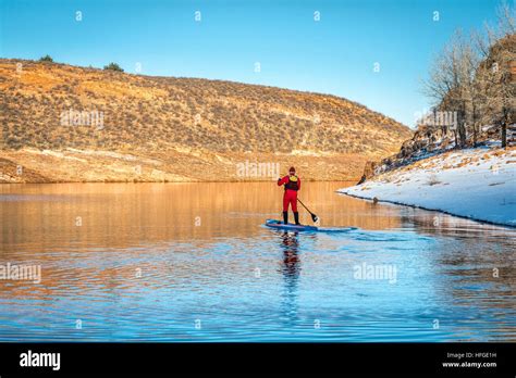 male paddler in red drysuit is paddling a stand up paddleboard on