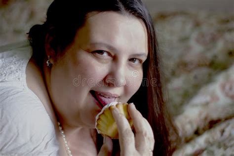 A Fat Woman In White Lies On The Bed And Holds Two Cakes In Her Hands