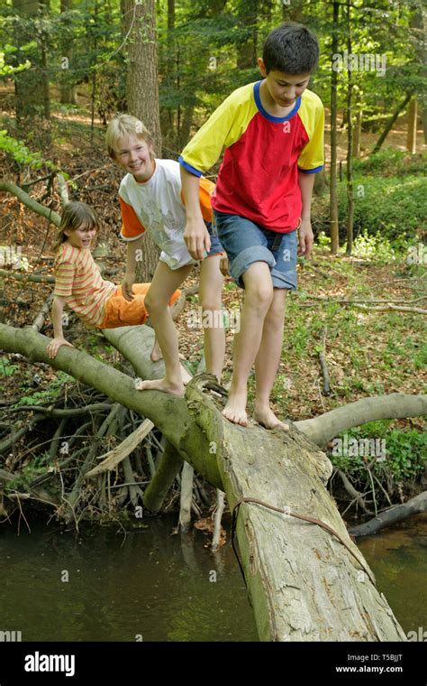 Young Boy Walking Barefoot Over A Tree Trunk That Is Lying Across A