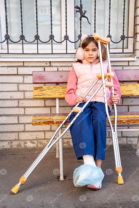 A Teenage Girl With A Broken Leg And Crutches Sits On A Bench Stock