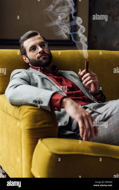 Handsome Bearded Young Man Smoking Cigar On Sofa Stock Photo Alamy