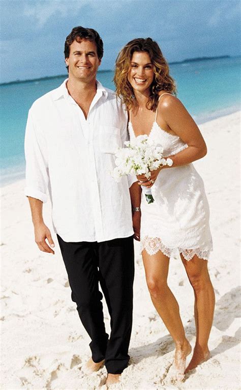 A Man And Woman On The Beach Posing For A Photo With Flowers In Their Hand