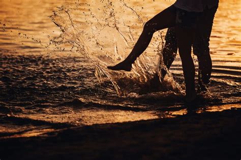couple splashing their feet in the water at sunset premium photo